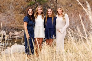 Four people in navy and white outfits pose together against a backdrop of tall golden grass and stone cliffs.