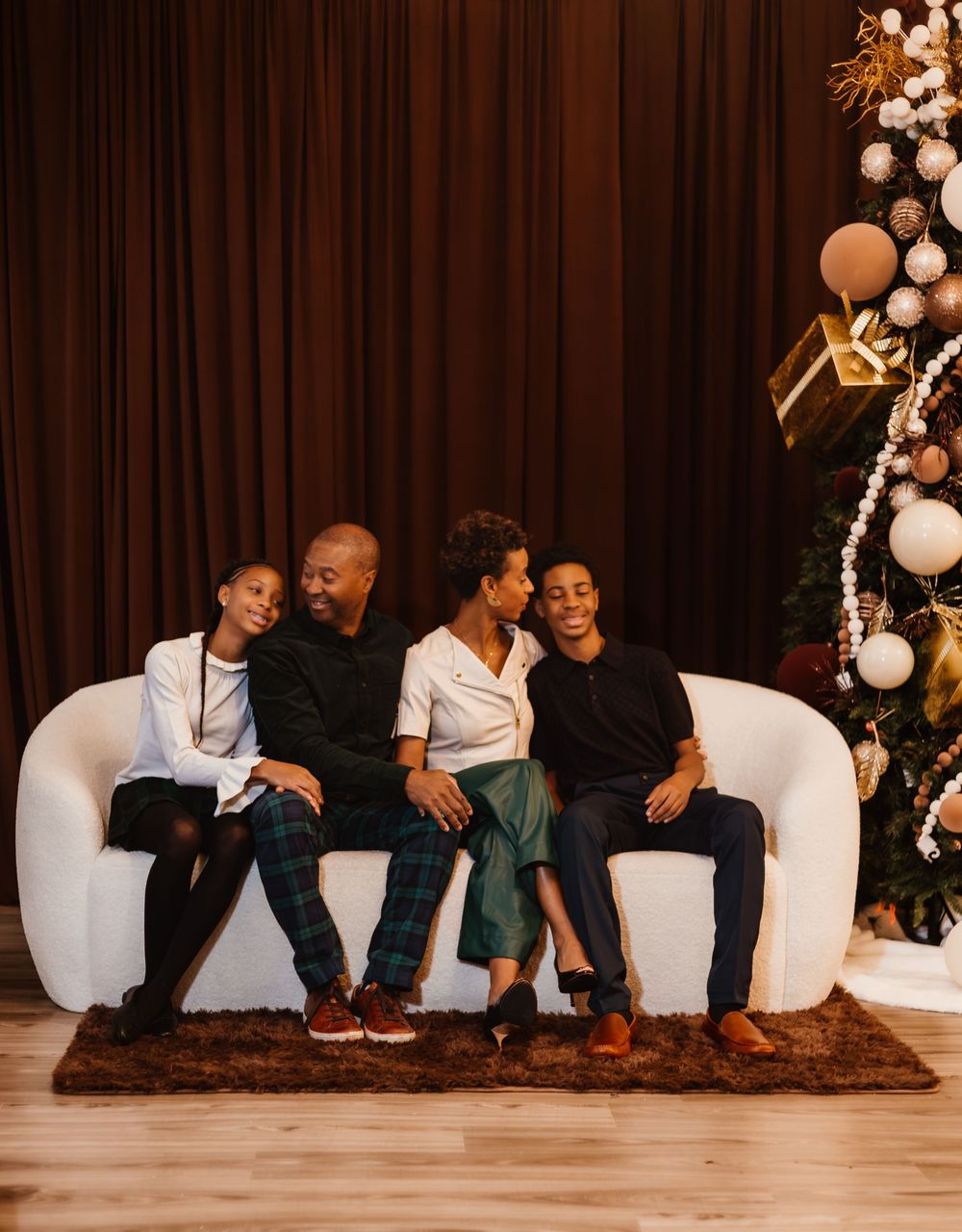 Family shares joyful moments together while sitting on white chairs against a dark backdrop with festive decorations.