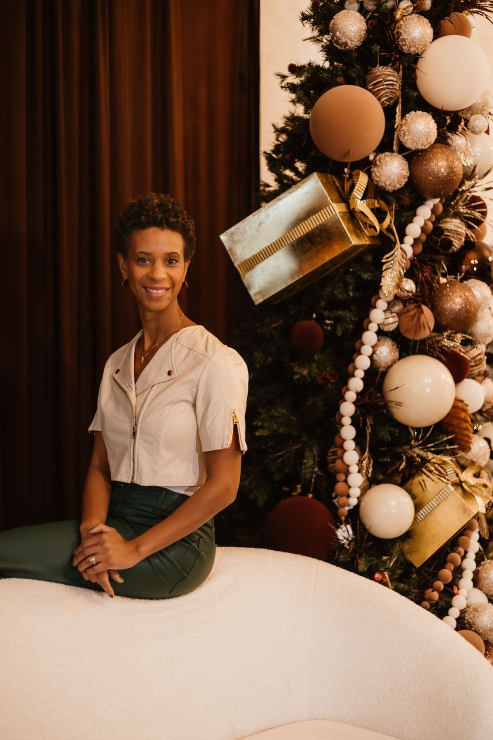 Elegant holiday scene with decorated Christmas tree featuring white ornaments, gold presents and pearls against warm lighting.