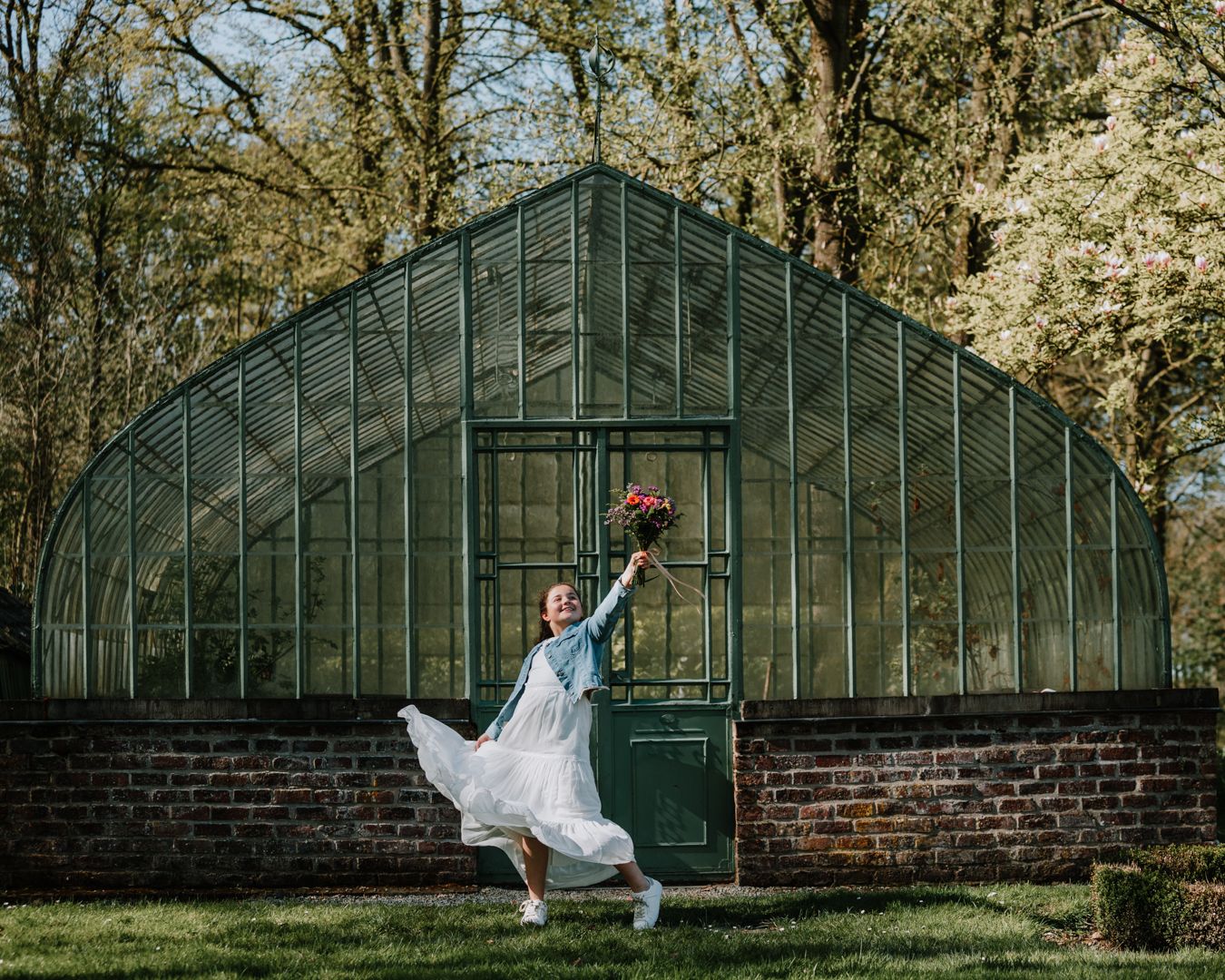 Vrolijk portret van een kind met bloemen voor een Serre. Foto voor een communie of lentefeest aan het Kasteel Van Ooidonk.