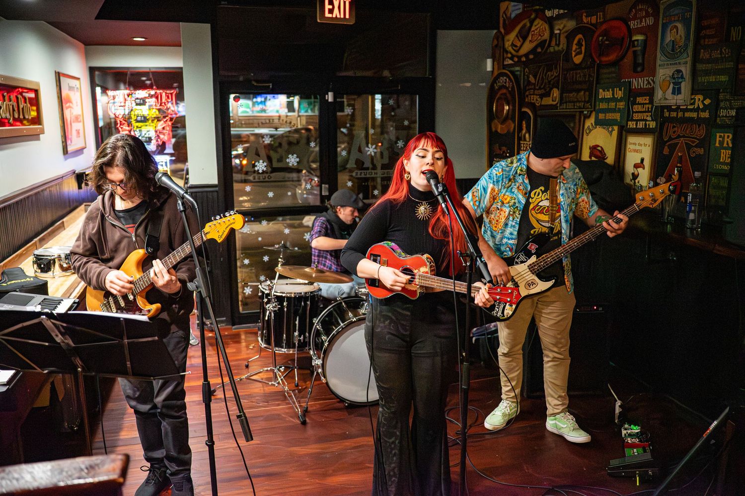 Musicians performing on stage in a dimly lit bar with vintage decor and posters on the walls.