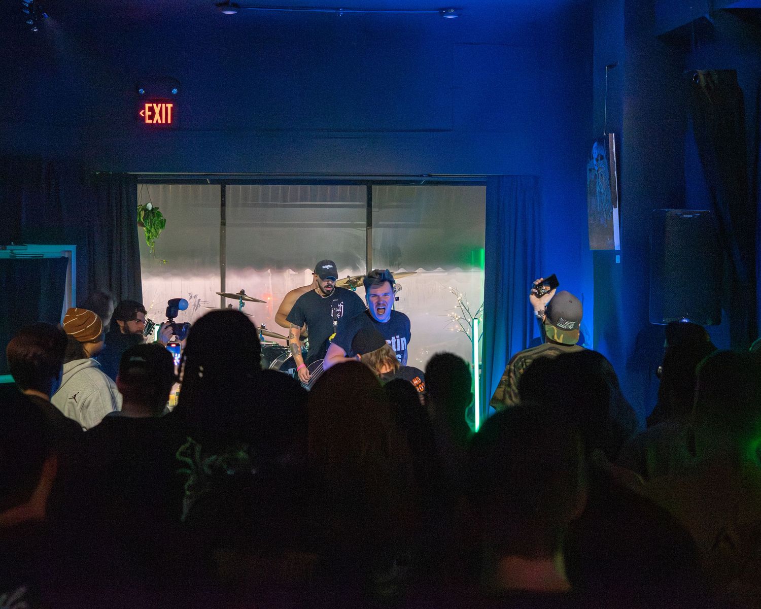 Dark concert venue with blue lighting and silhouetted audience members.