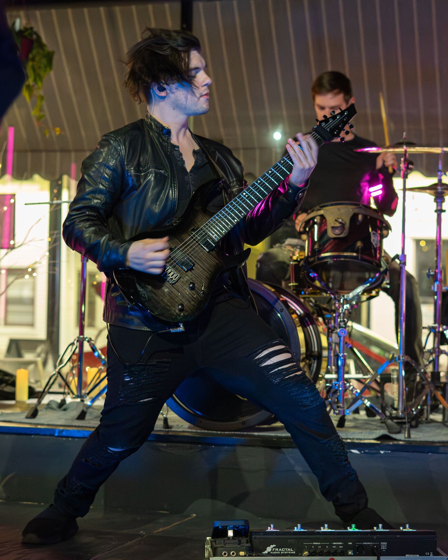 Guitarist in dark attire performs dynamic stage moves during energetic concert performance.