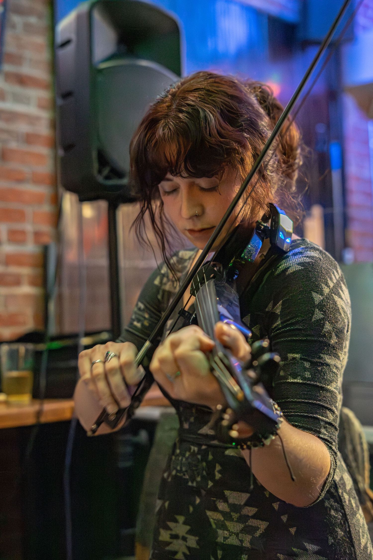 Violinist performs with intense focus in dimly lit venue with brick wall background.