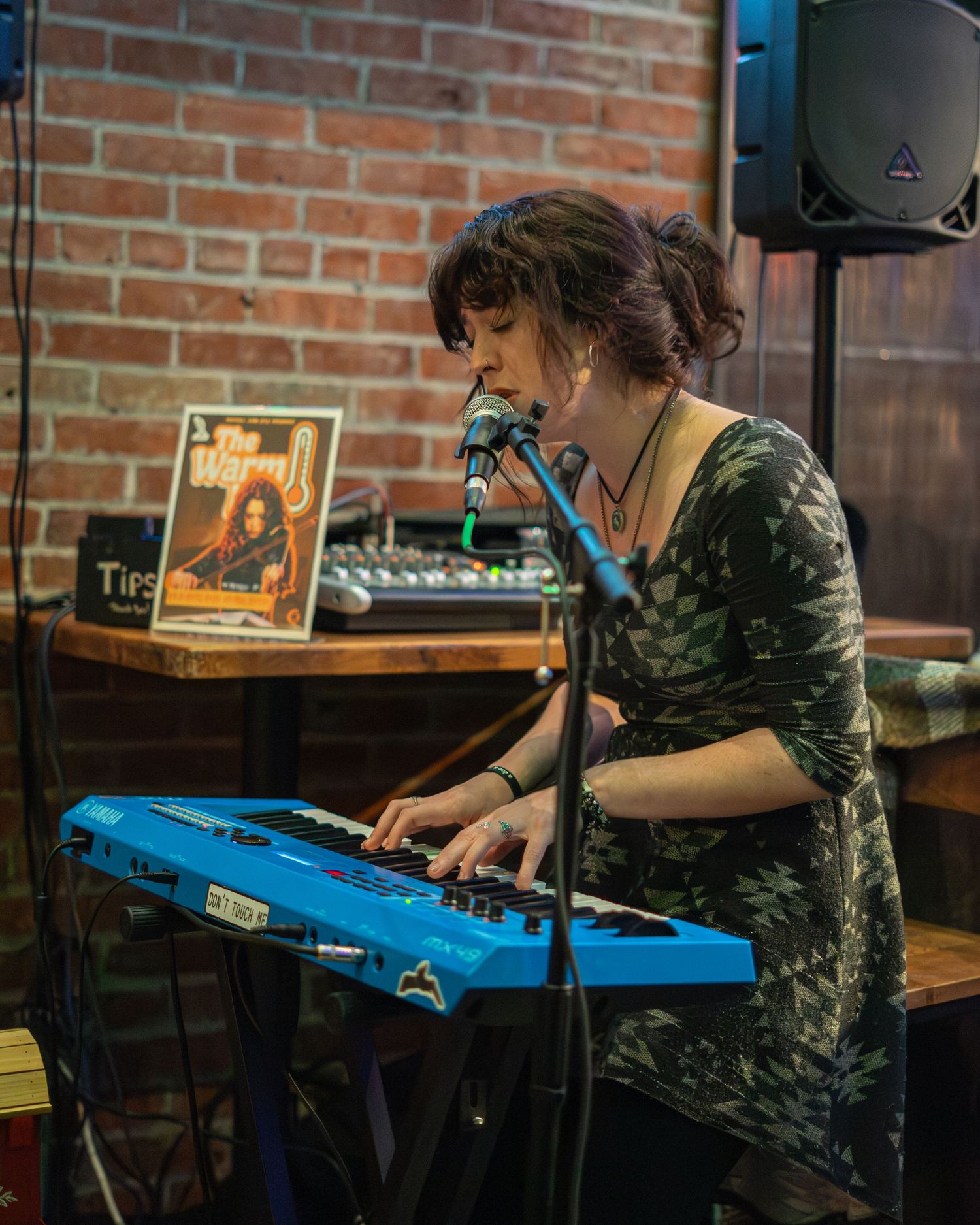 Musician plays bright blue keyboard against brick wall backdrop in intimate venue setting.