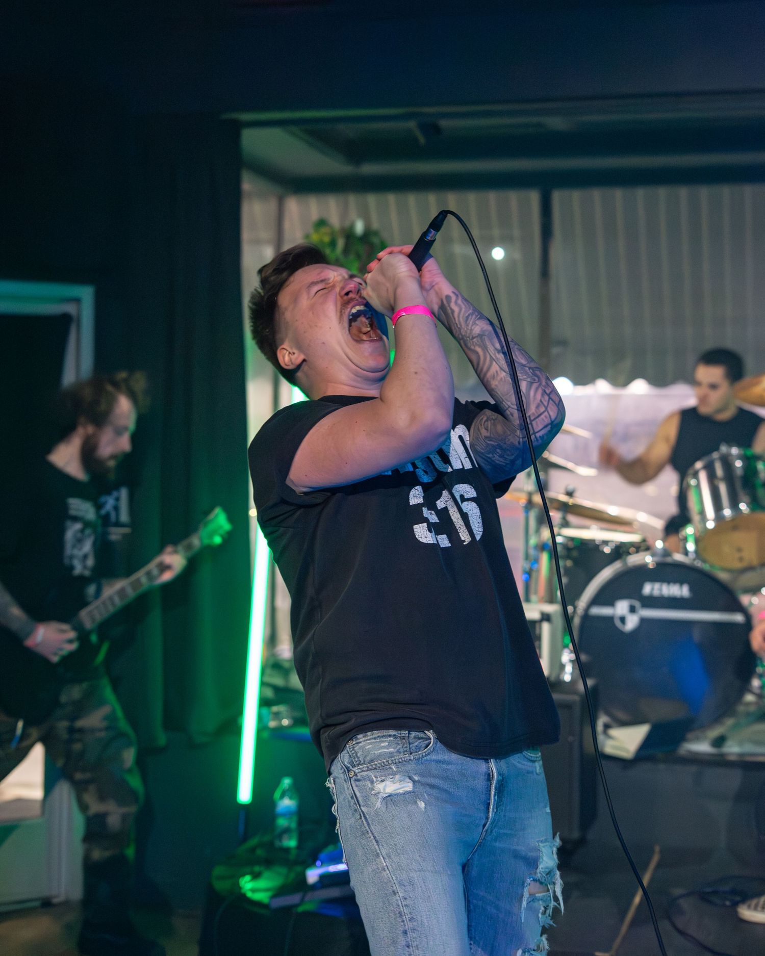 Rock band vocalist performs energetically on stage with dramatic lighting and band members in the background.