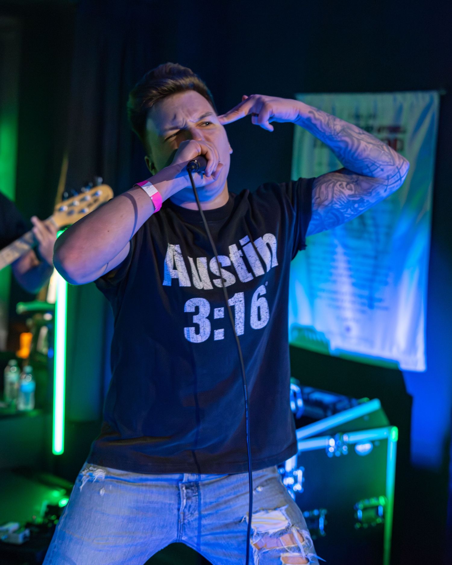 Vocalist in black tank top singing passionately during live performance with blue and green stage lighting.