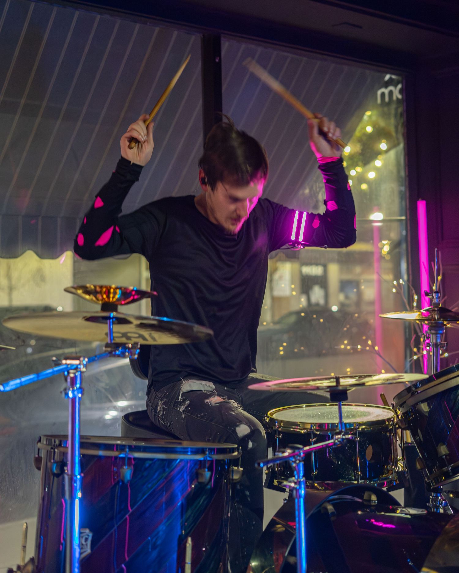 Drummer performing on stage with illuminated drum kit under purple and blue lighting effects.