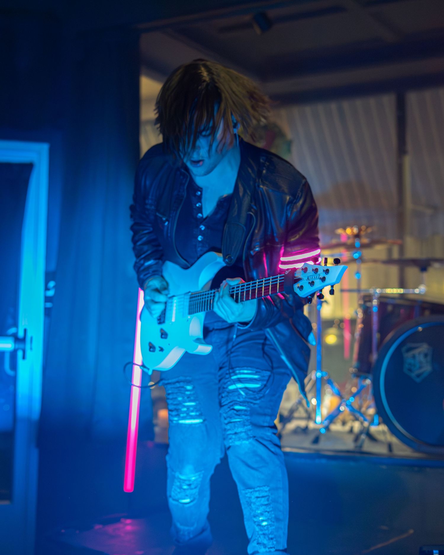 Musicians performing on stage with dramatic blue neon lighting and atmospheric effects.