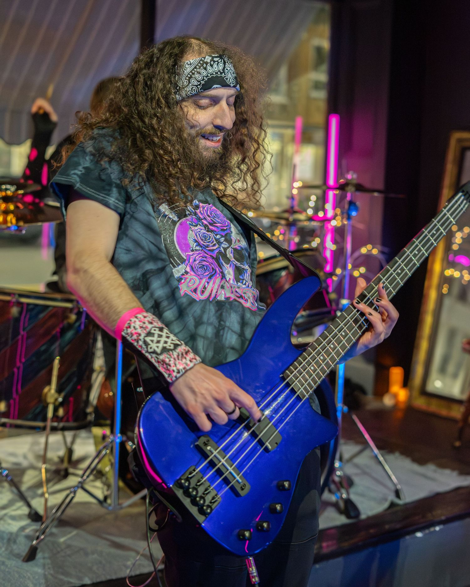 Bass player with long hair performs on bright blue electric bass guitar during live concert.