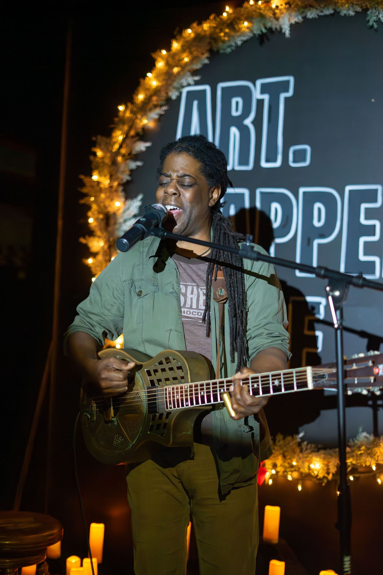 Musician performing with acoustic guitar under string lights and holiday decorations.