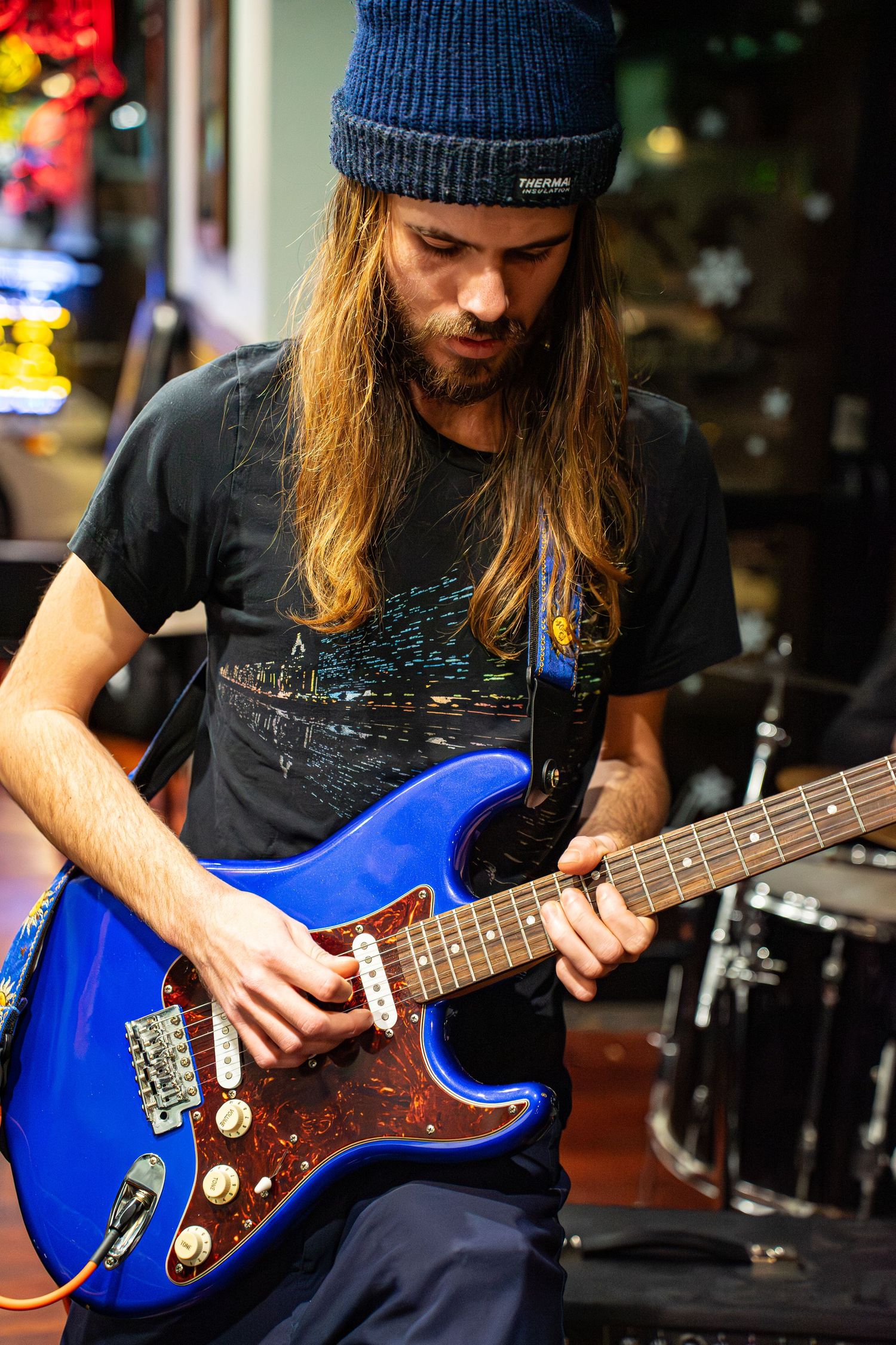Musician playing blue electric bass guitar while wearing beanie hat.