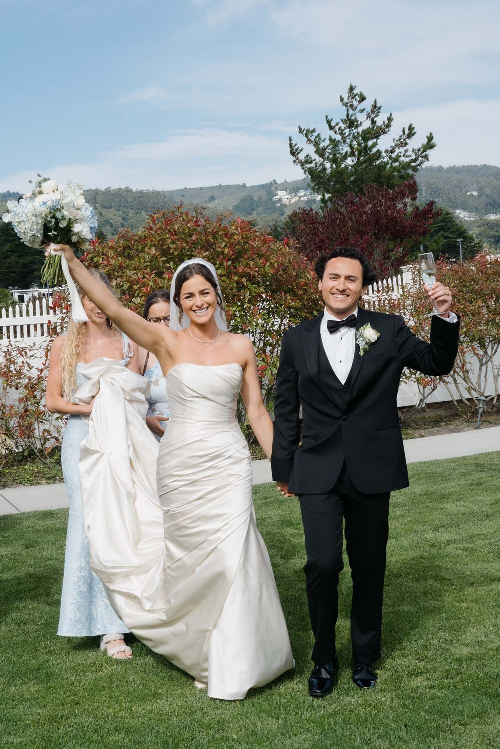A wedding celebration on a manicured lawn with a white picket fence and mountain scenery in the background.