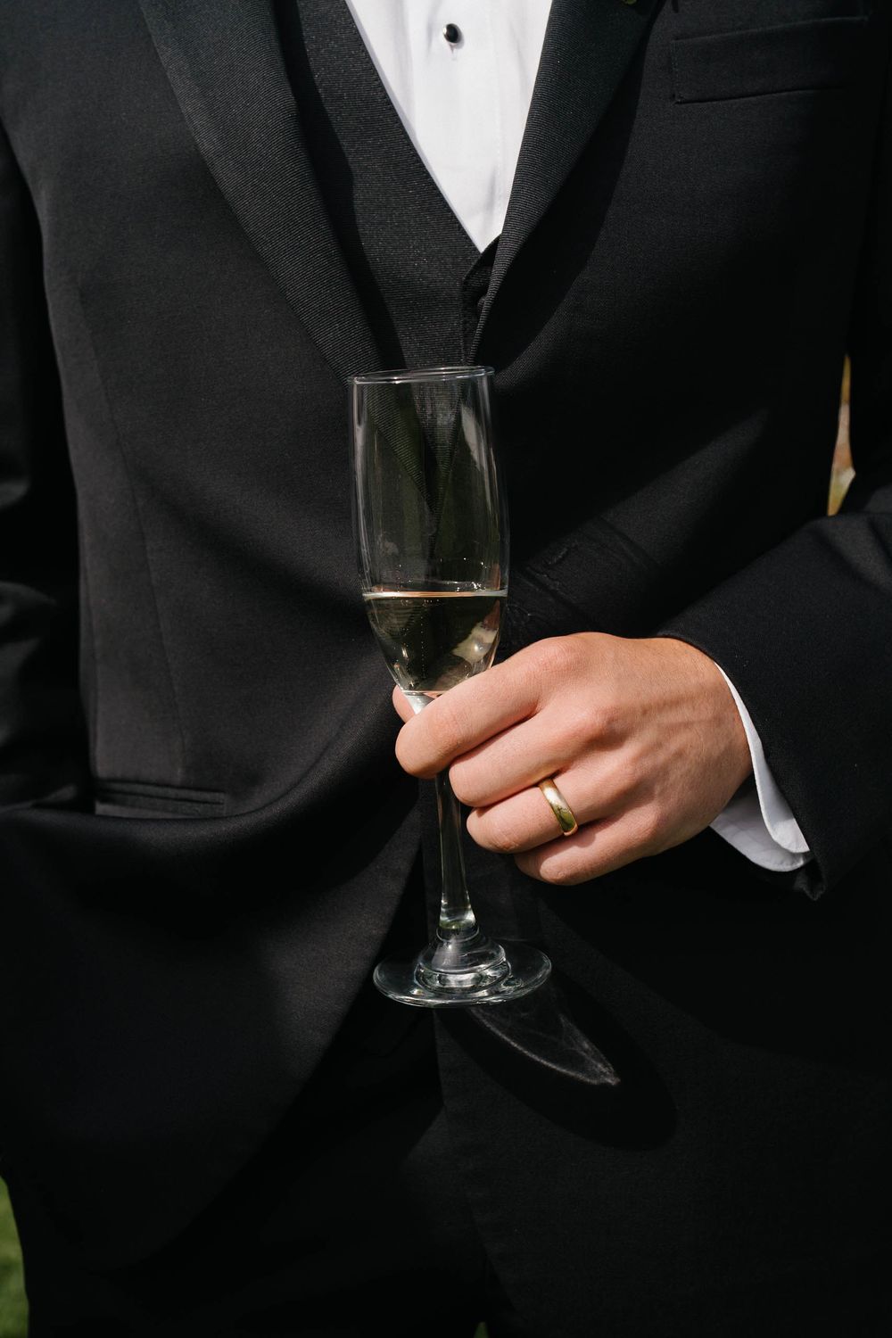 Person in formal black tuxedo holding a glass of champagne or wine at an elegant event.