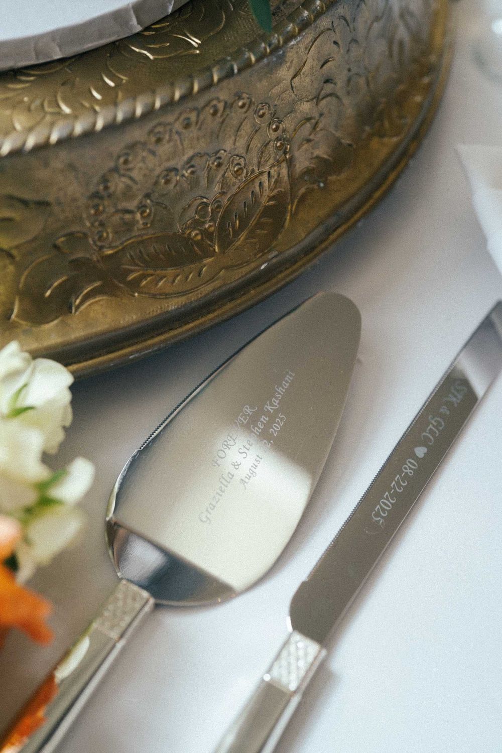 Ornate brass or gold serving platter with elegant silverware arranged on a white tablecloth.