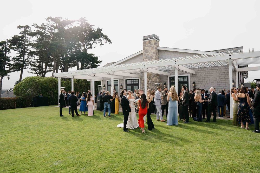 Wedding guests gather outside a white tent pavilion on a green lawn during an outdoor celebration.