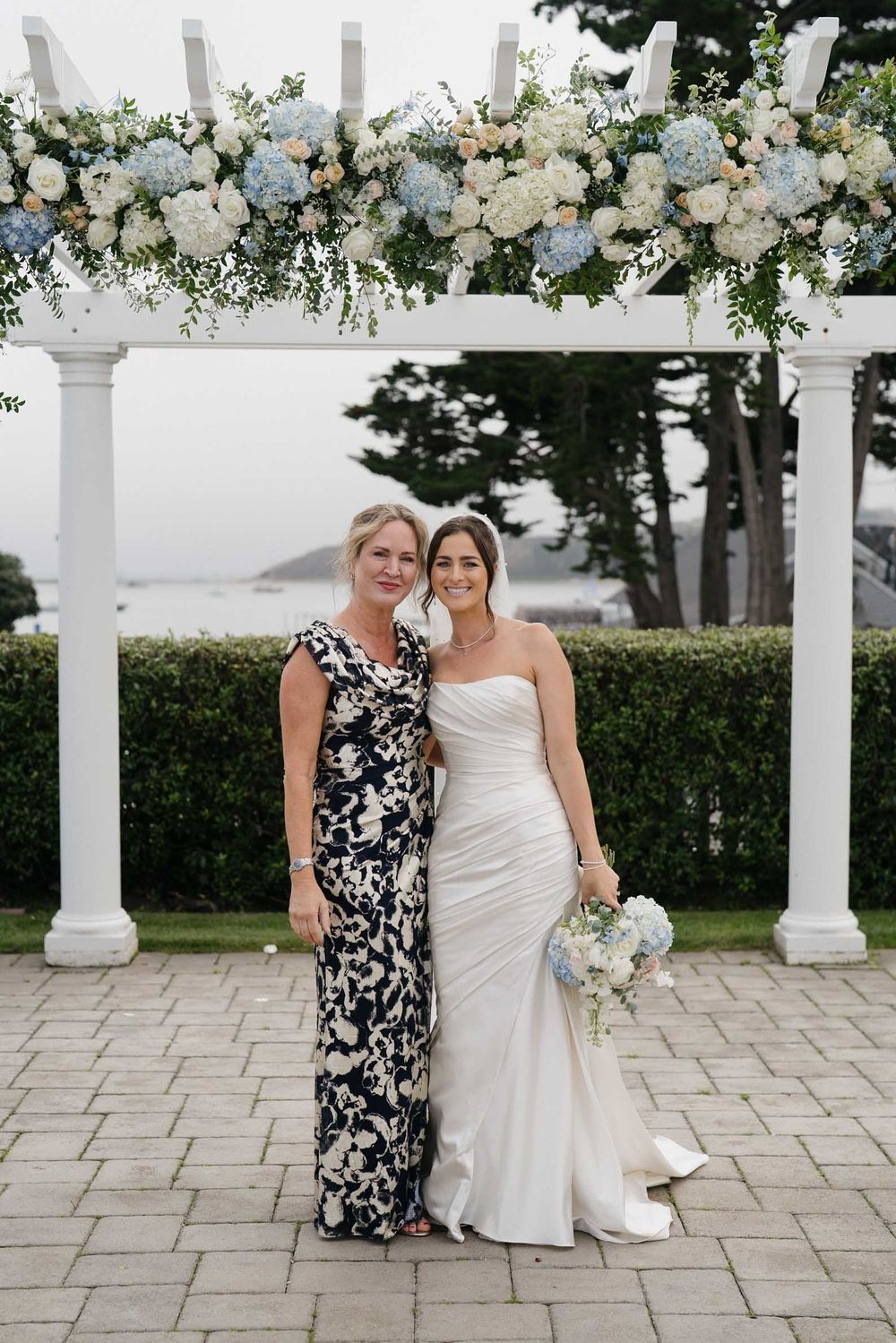 A wedding ceremony setup with white floral arrangements decorating a columned pergola.