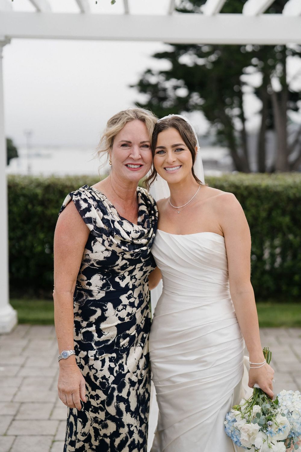 Wedding party members in black and white dresses pose together on a stone patio.
