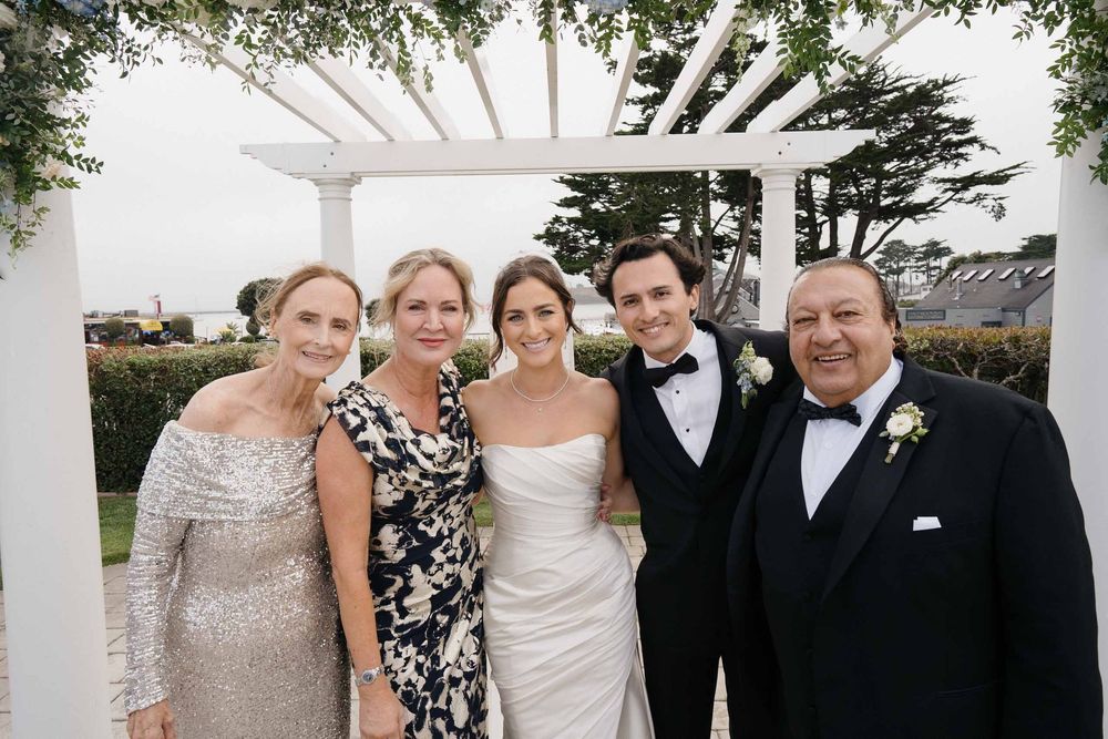 Wedding party poses together under a white pergola with greenery and decorative flowers.