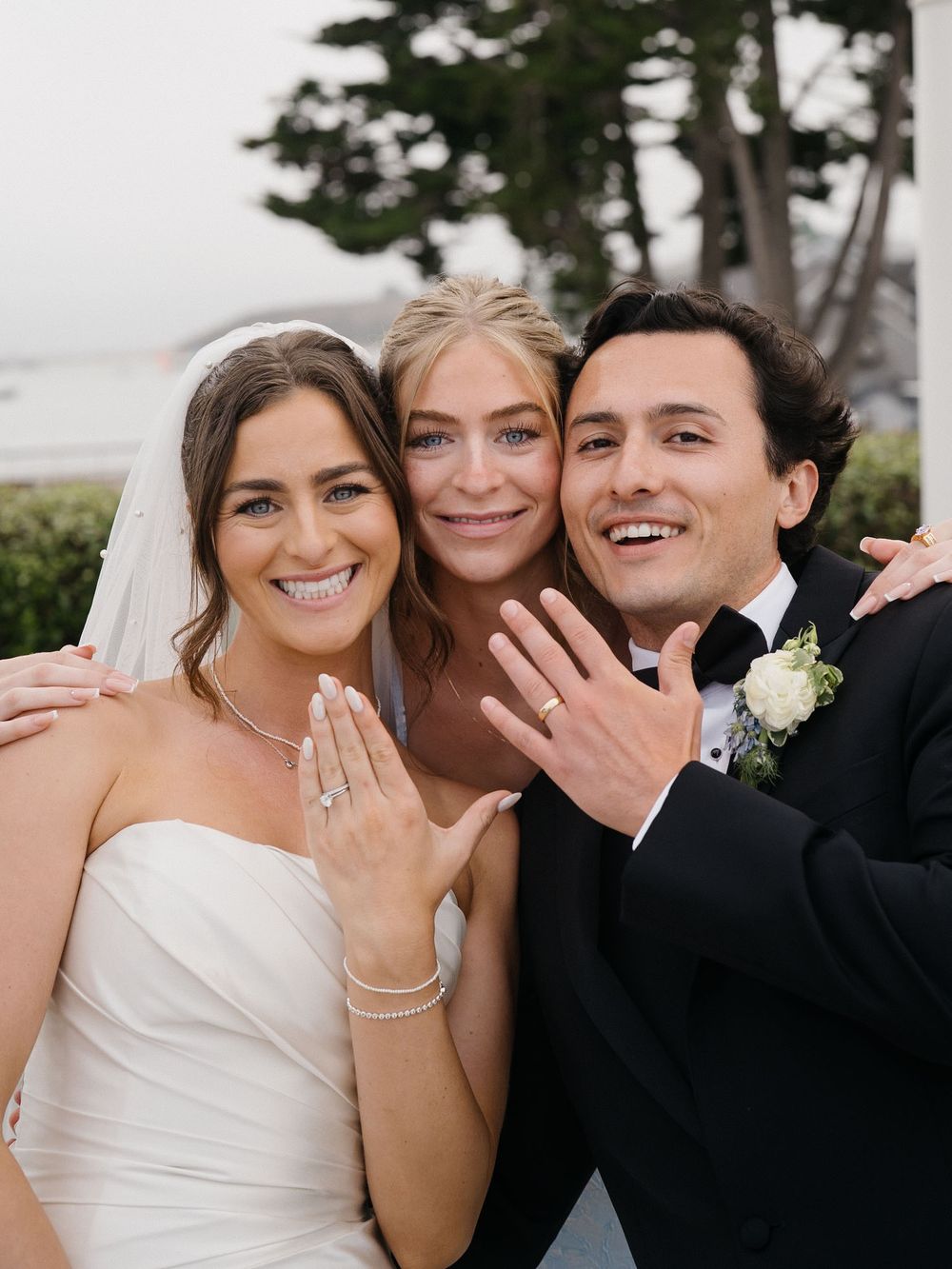 Wedding party members smiling and showing off their rings in an outdoor setting.
