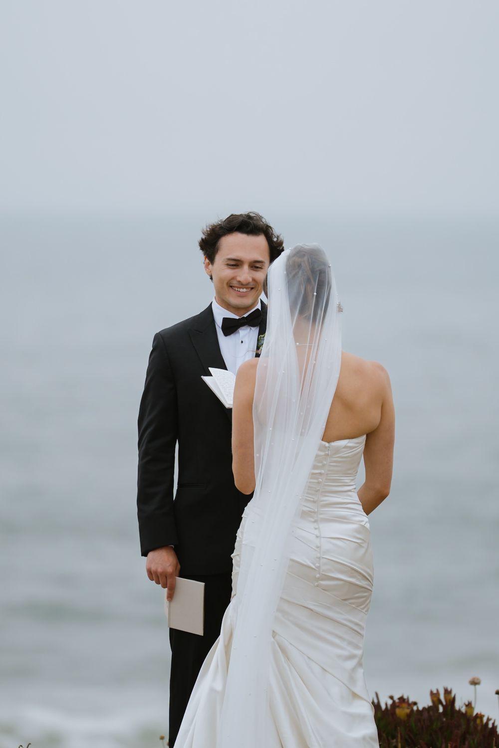 Wedding couple posing for romantic photos against a misty coastal backdrop.