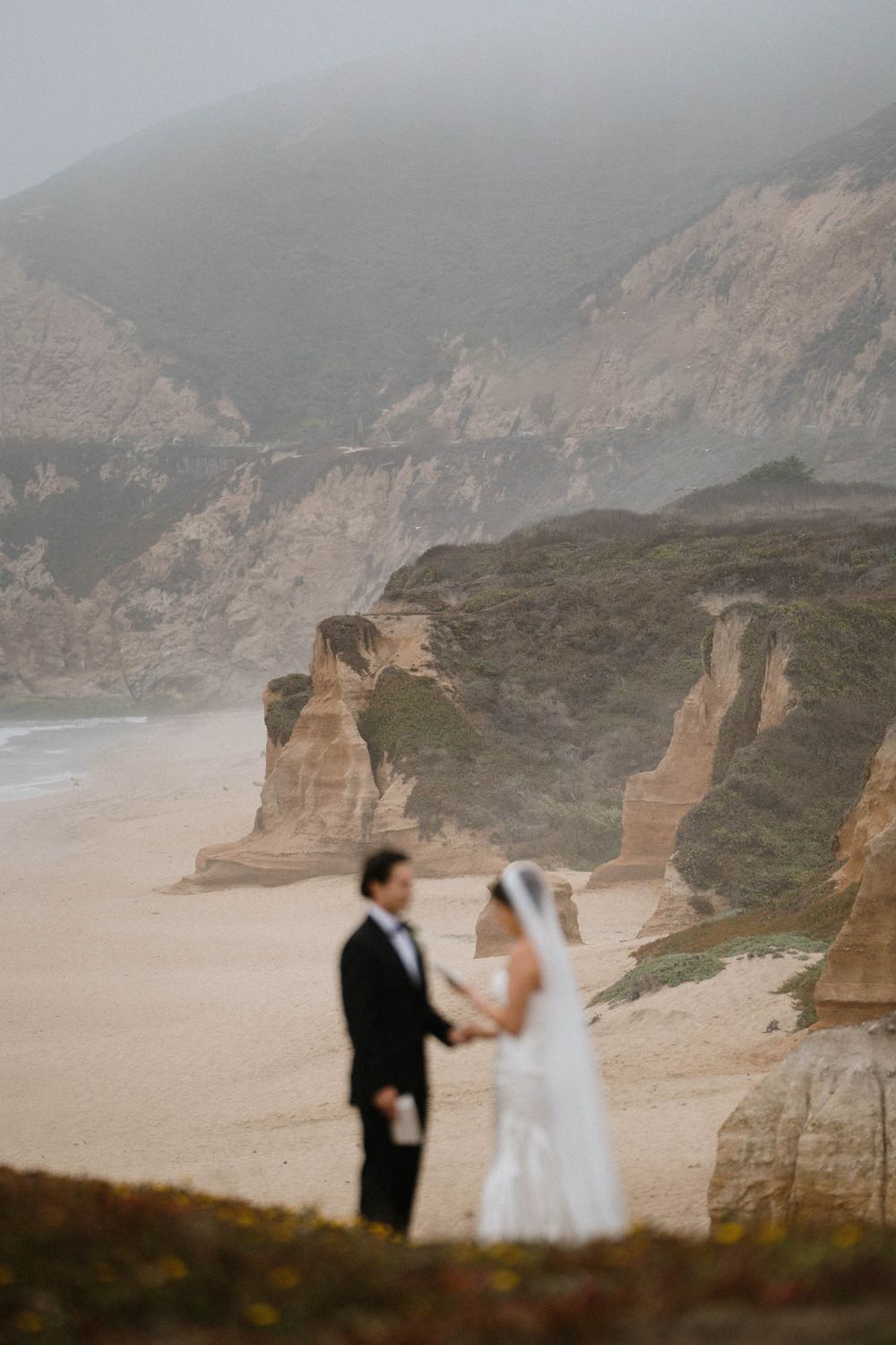 Dramatic coastal cliffs overlooking a foggy beach during a wedding photoshoot.