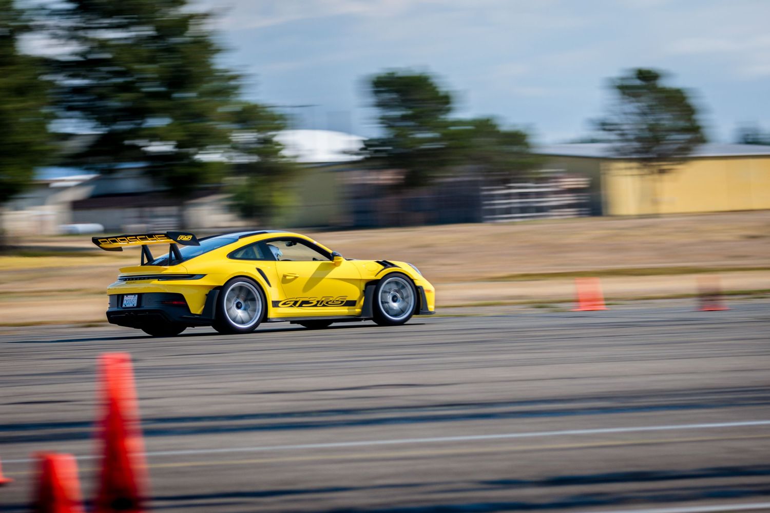 A bright green Porsche sports car speeds past in motion blur on a wet racetrack.