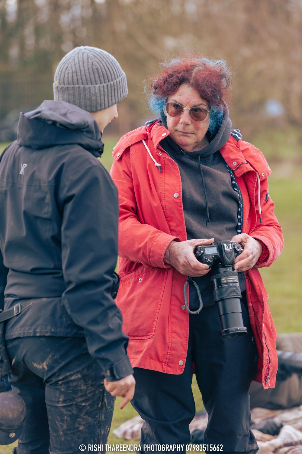 Two photographers reviewing photos on a camera outdoors on a cold day while wearing winter jackets.