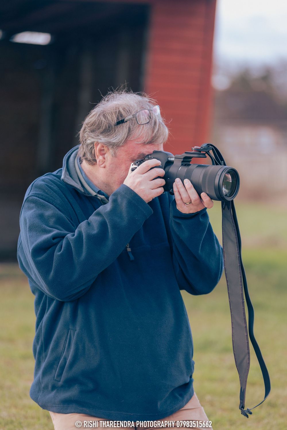 A photographer in a navy blue jacket takes multiple photos in sequence while holding a camera outdoors.