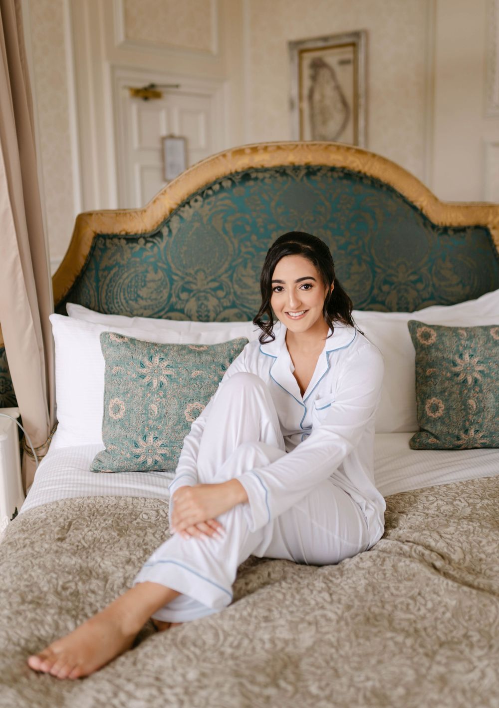 White bedroom interior with teal headboard and decorative pillows on a luxurious bed.