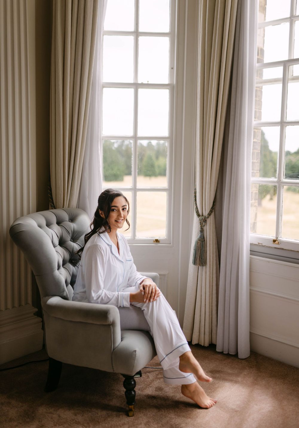 Bright room with gray tufted chair near windows with flowing curtains.