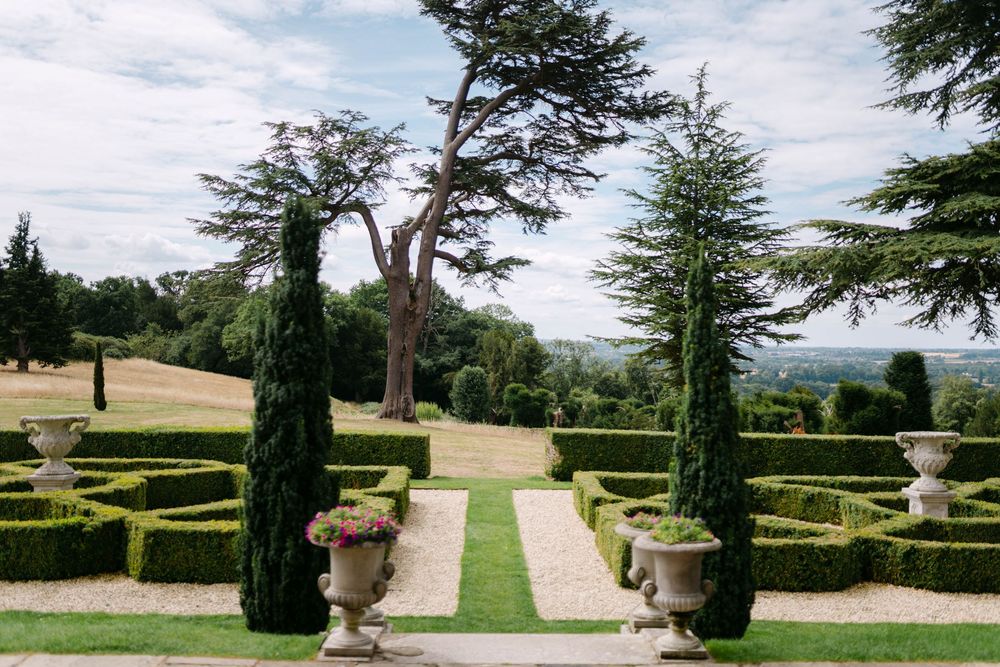 Formal garden path lined with cypress trees and decorative urns leading to a scenic view.