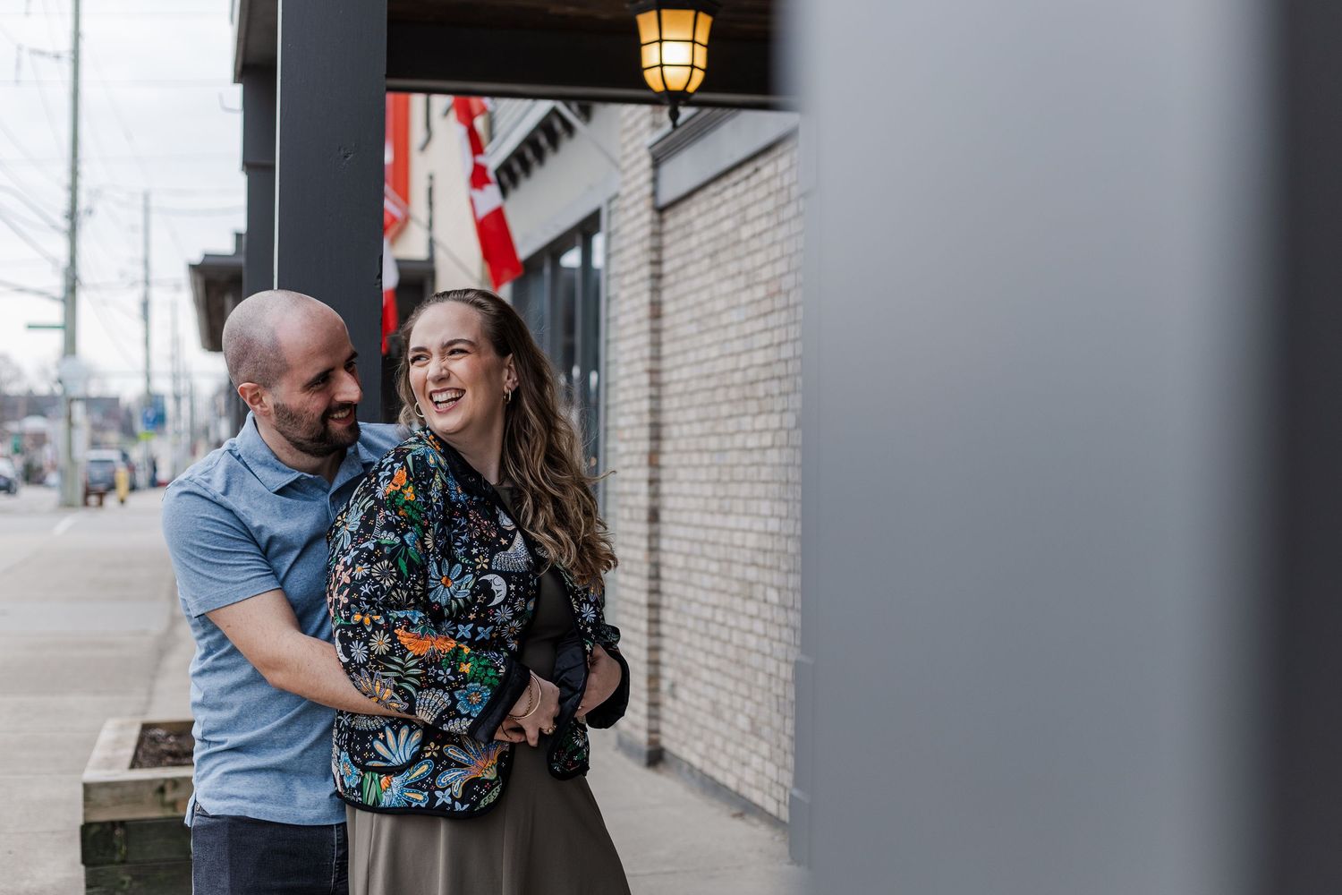 A couple shares a joyful moment together on a city sidewalk next to a brick wall.