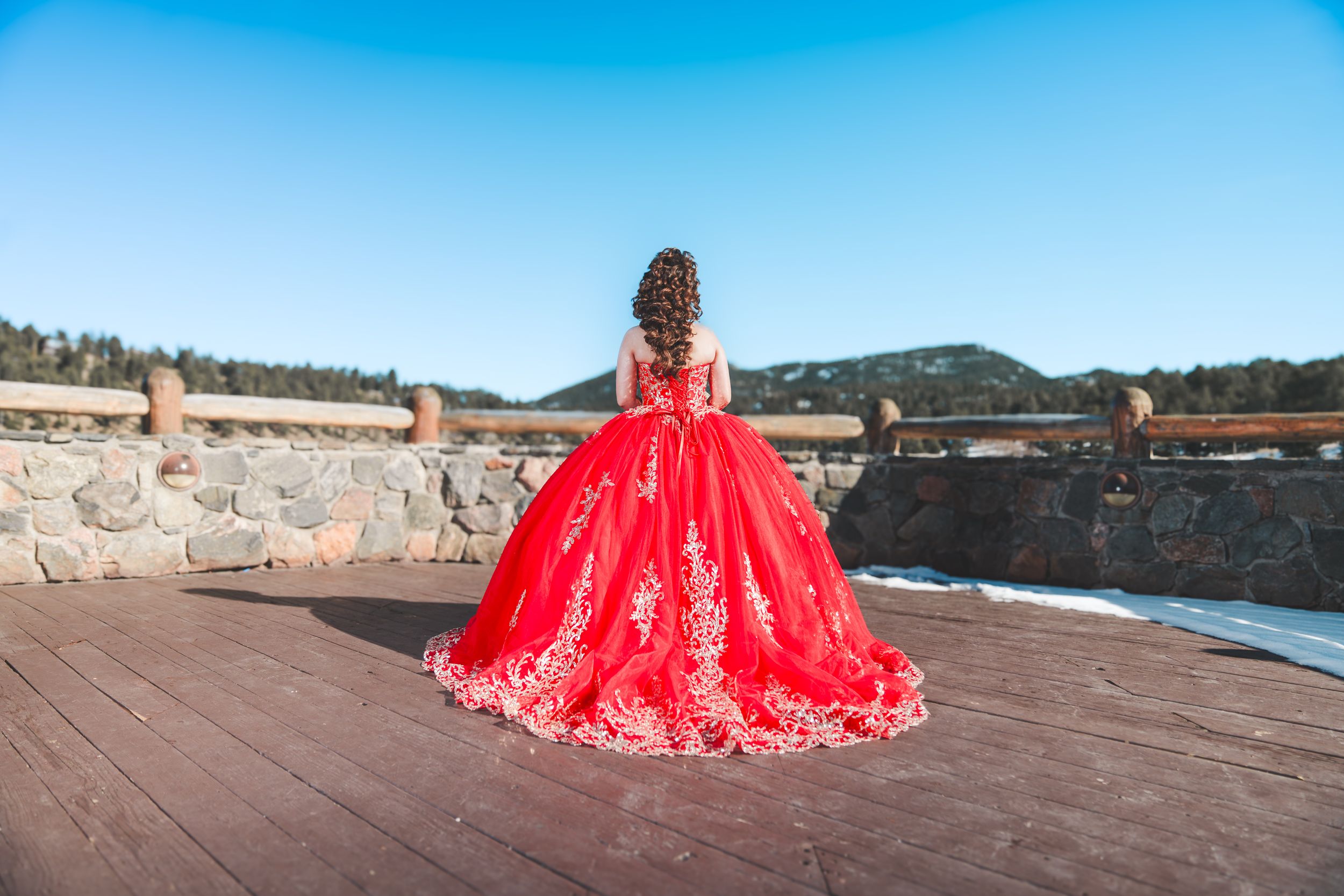 A flowing red ballgown dress creates a stunning contrast against the blue sky and coastal landscape backdrop.