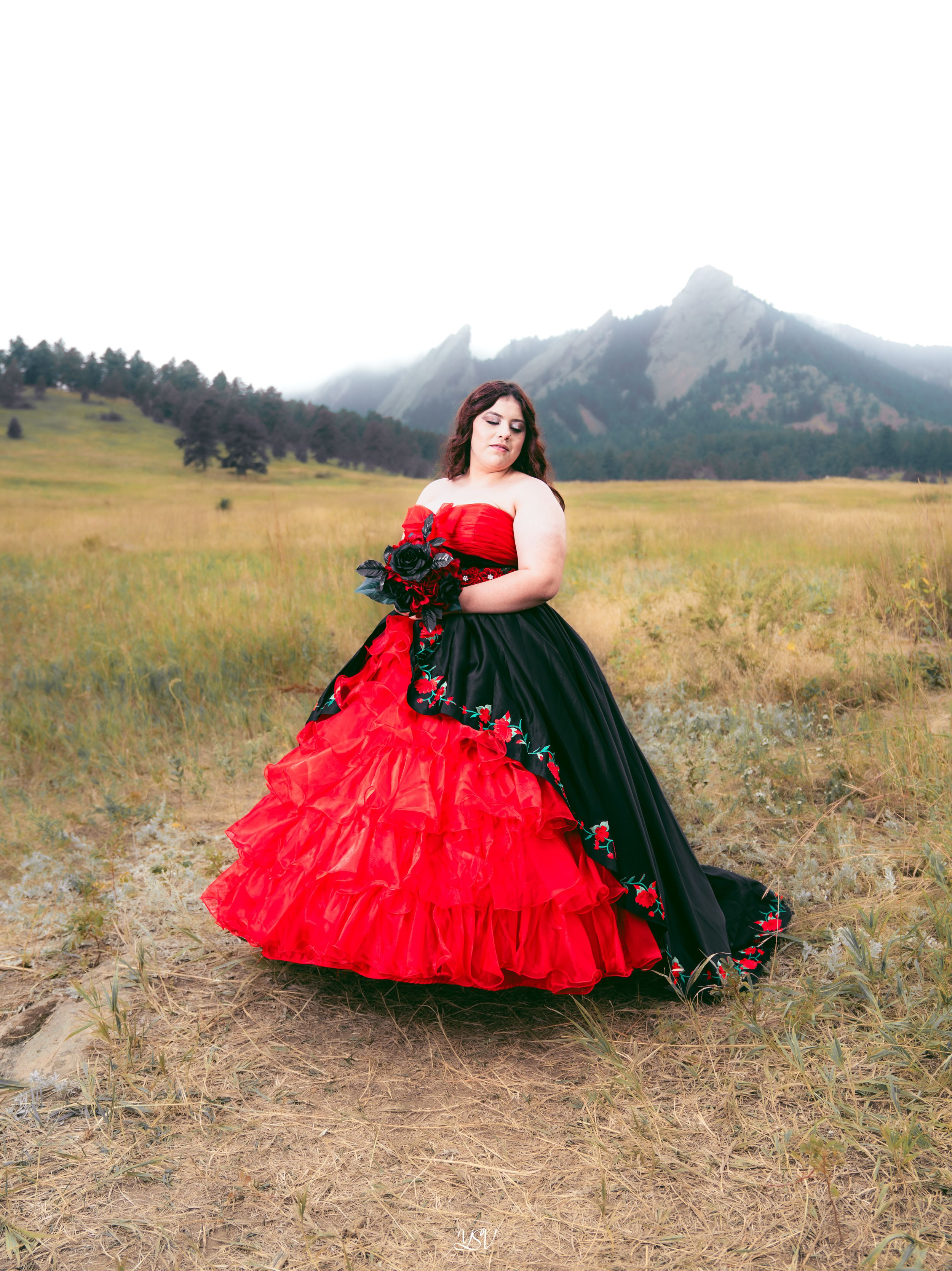 Two contrasting dresses, one red and one black, create a dramatic silhouette against a scenic mountain landscape.