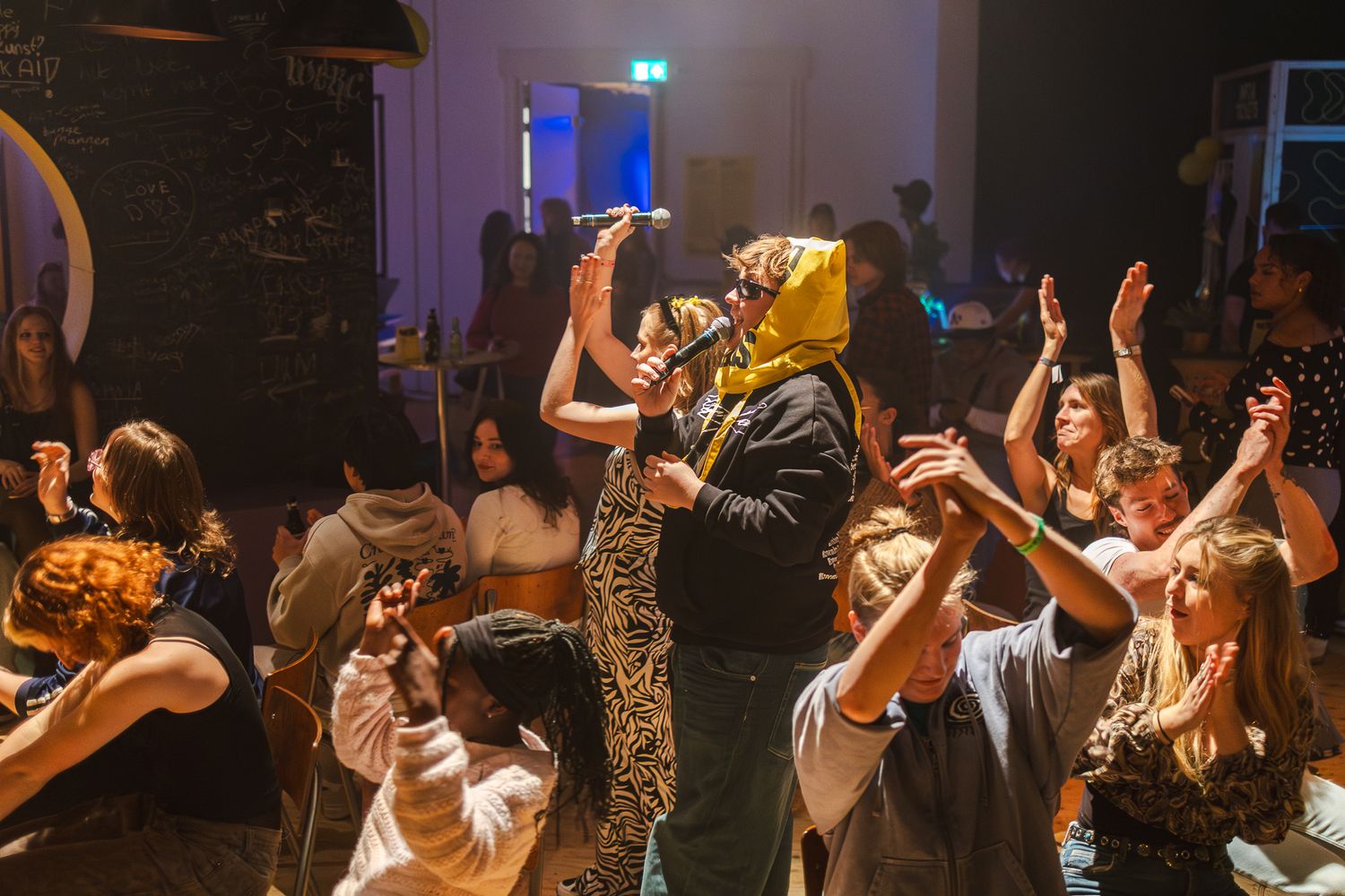 Crowd of concert attendees dancing with hands raised in a dimly lit venue with blue lighting effects.