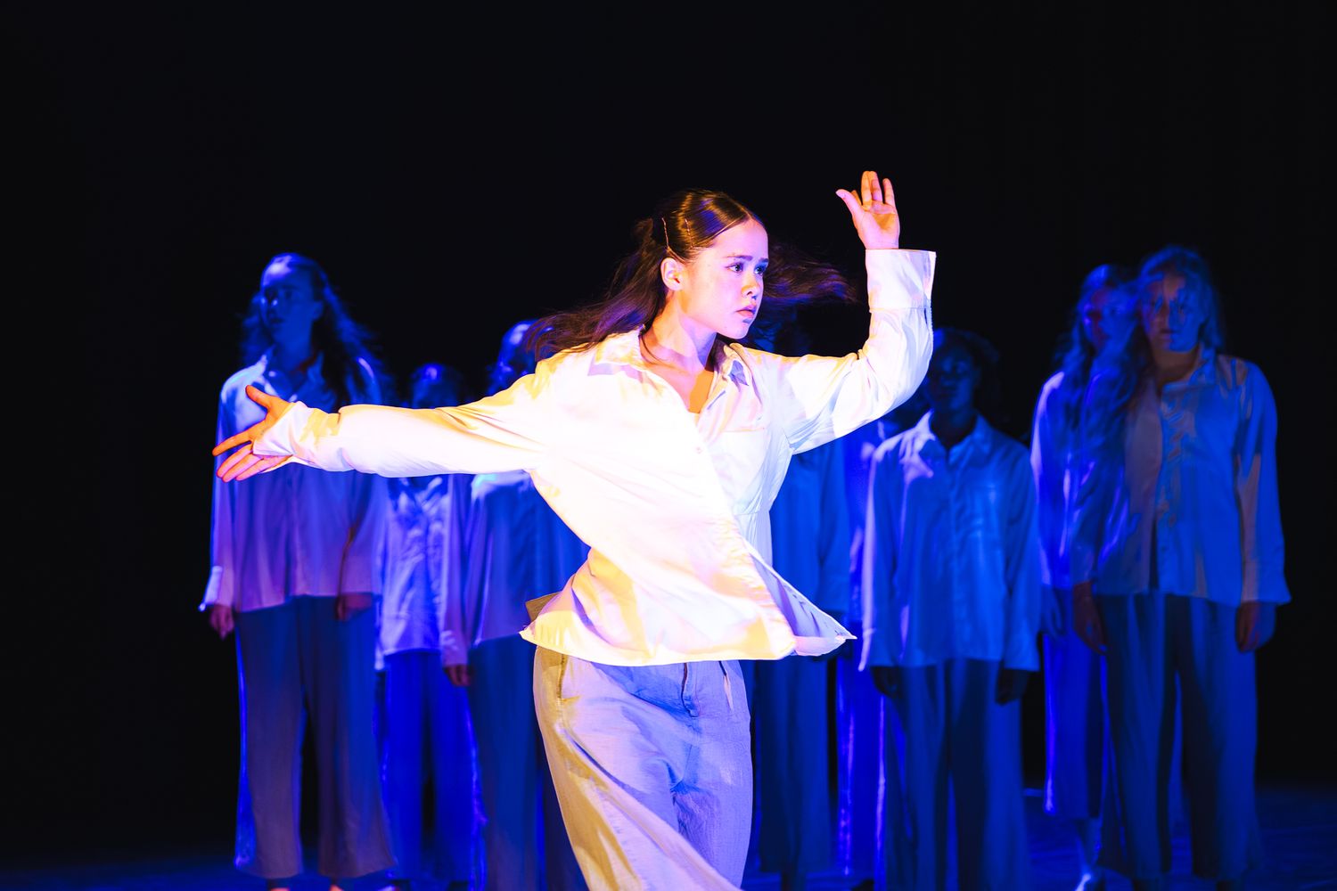 Dancers in white costumes perform an ethereal dance sequence against a dark background with blue lighting effects.