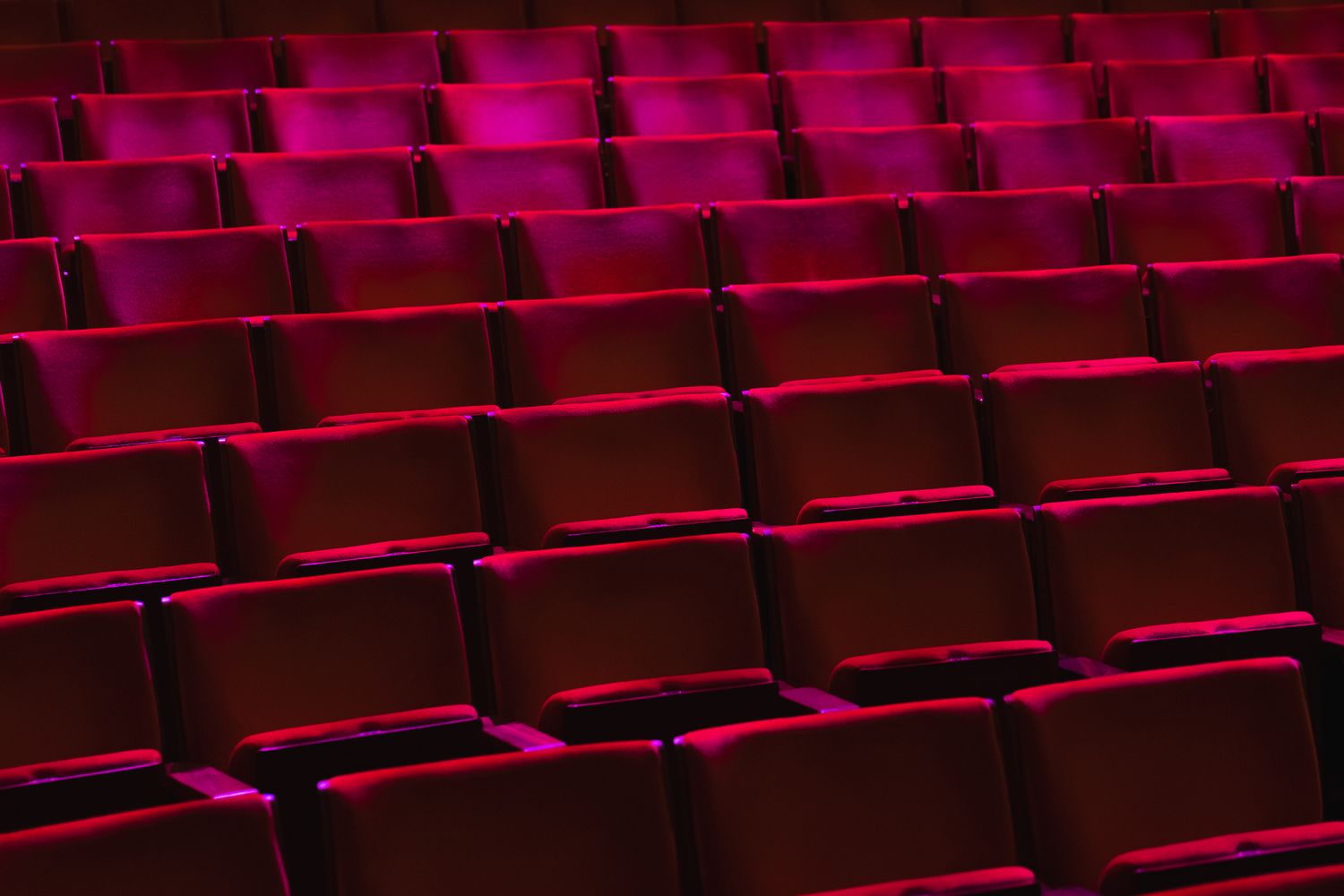 Empty red theater seats arranged in rows, perfect for events, performances, and entertainment venues.