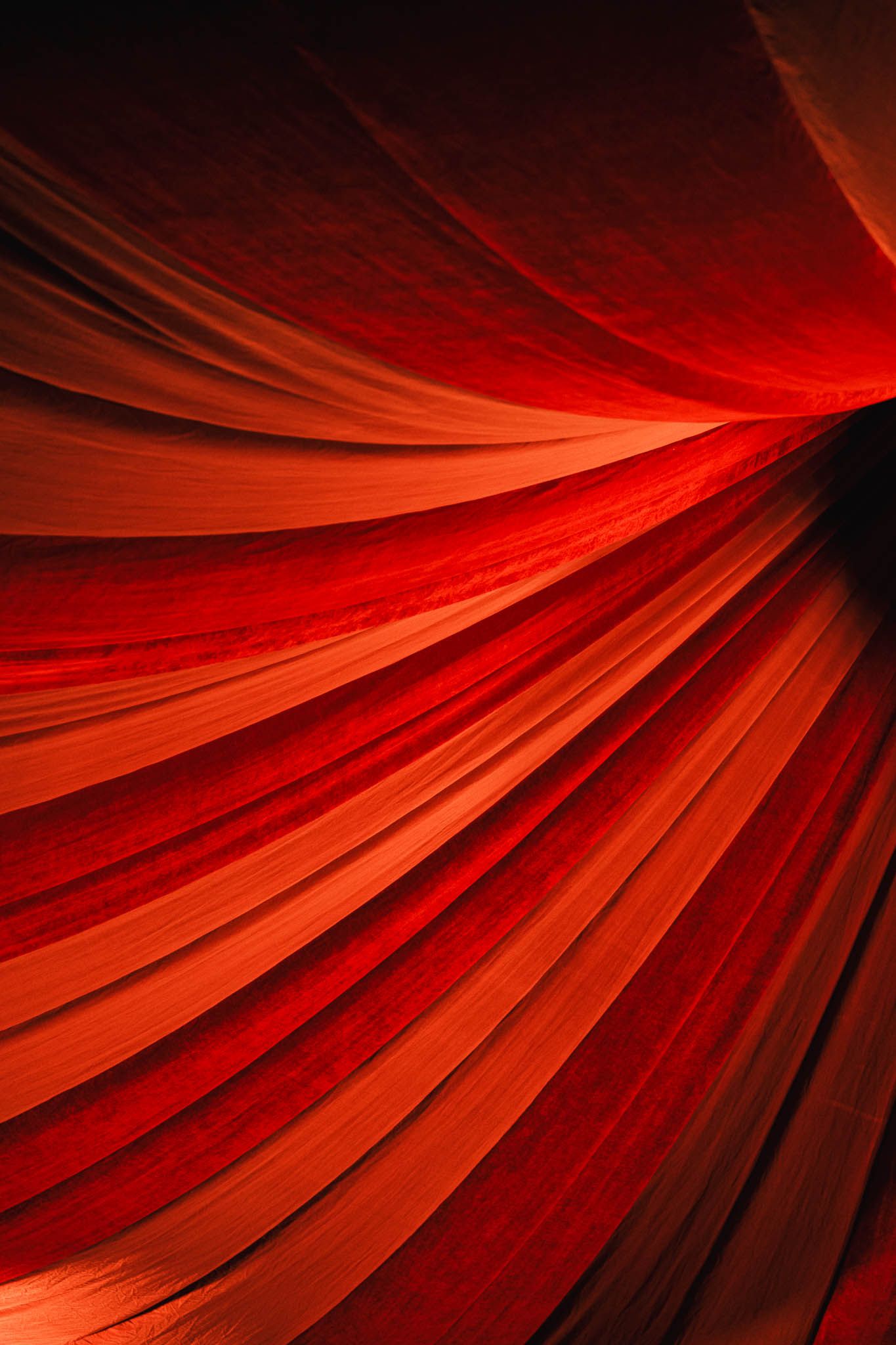 Abstract close-up of flowing red and orange fabric folds radiating from a dark center point.