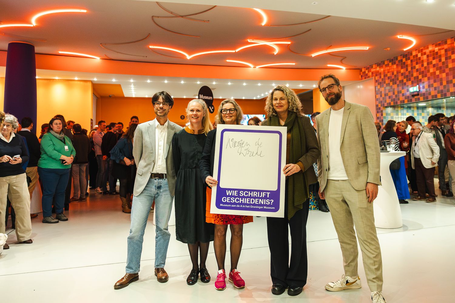 People wait in line at a crowded indoor venue with orange lighting and modern interior design.