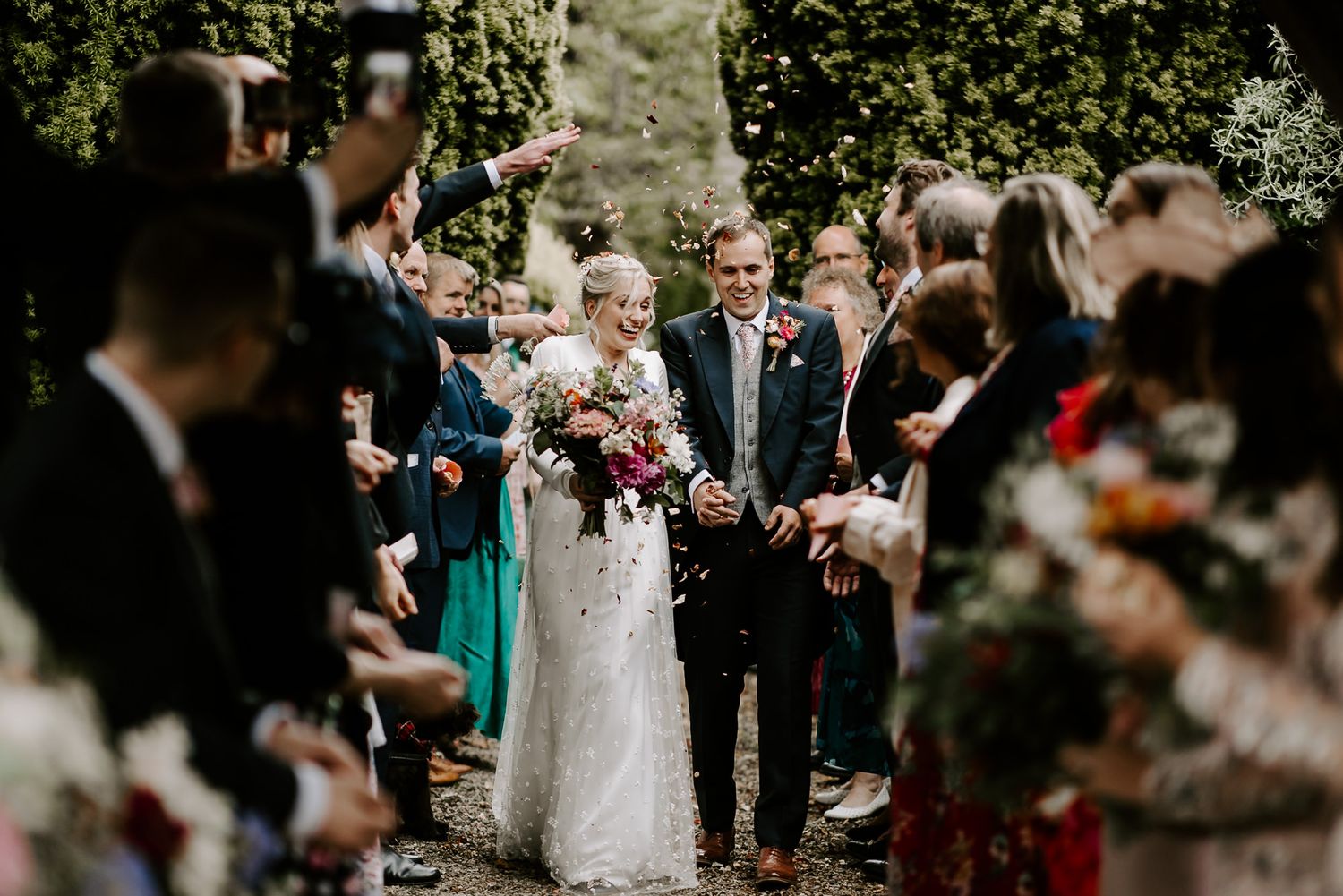 Wedding guests toss flower petals in celebration during an outdoor ceremony at a scenic mountain venue.