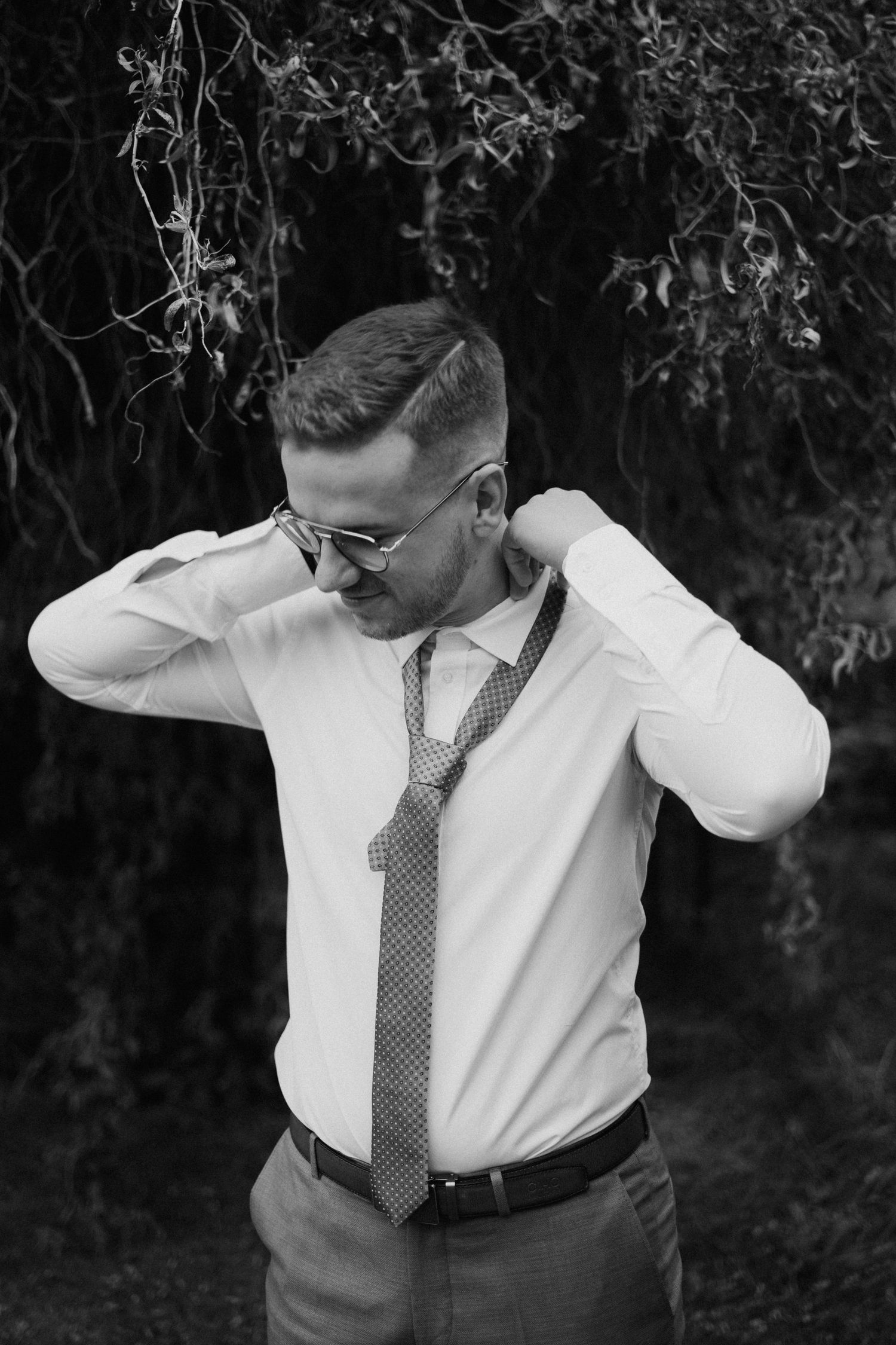 A person in formal attire adjusts their tie outdoors.