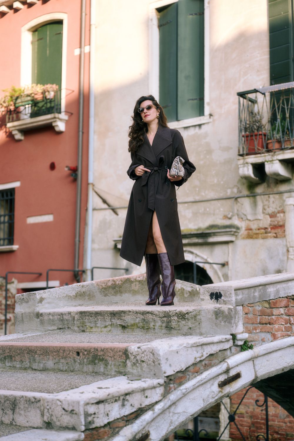 A person in black clothing stands on stone steps against a pink and white building facade in Venice.