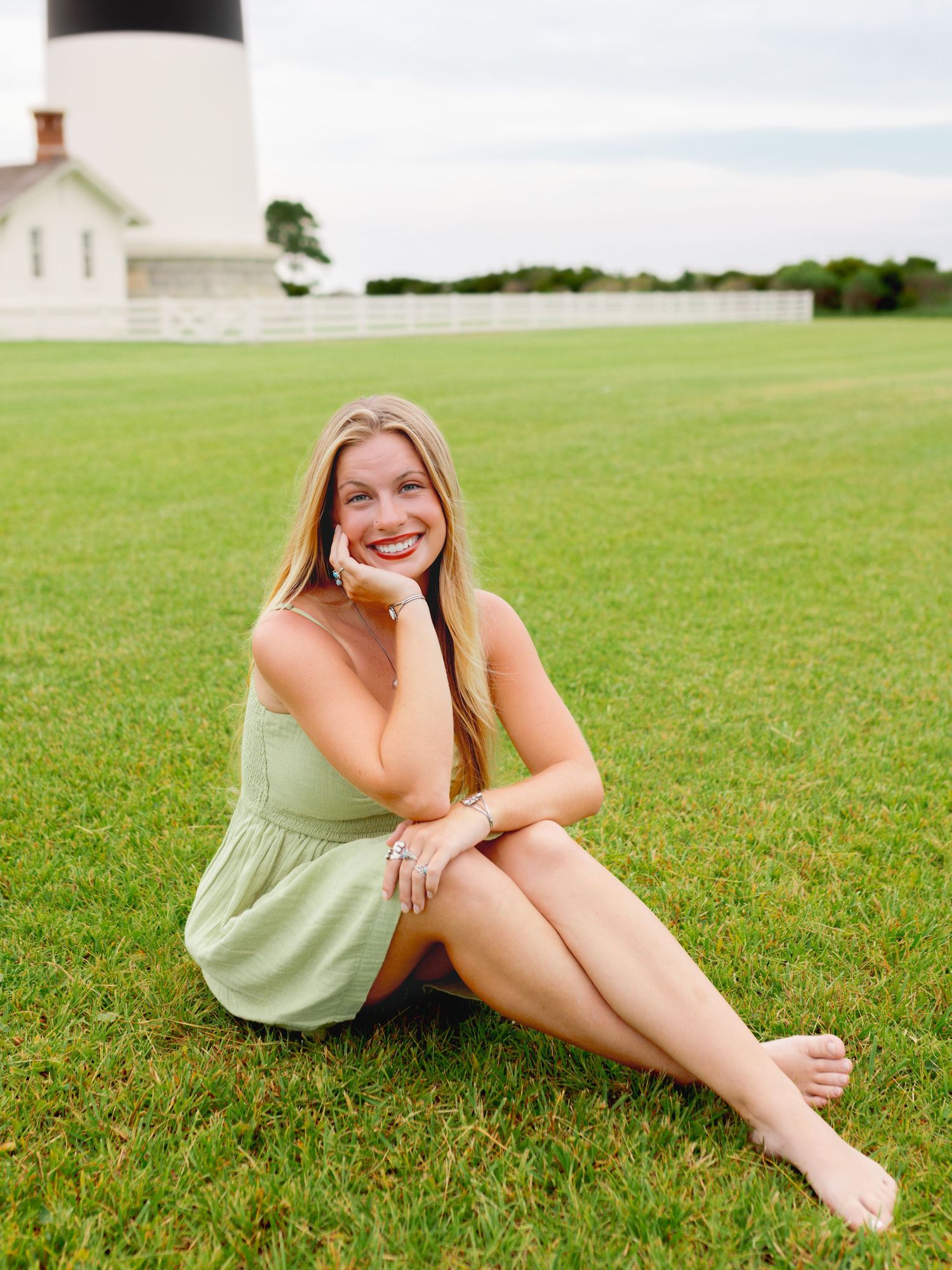 Woman in mint green dress sits on grass with lighthouse in background.