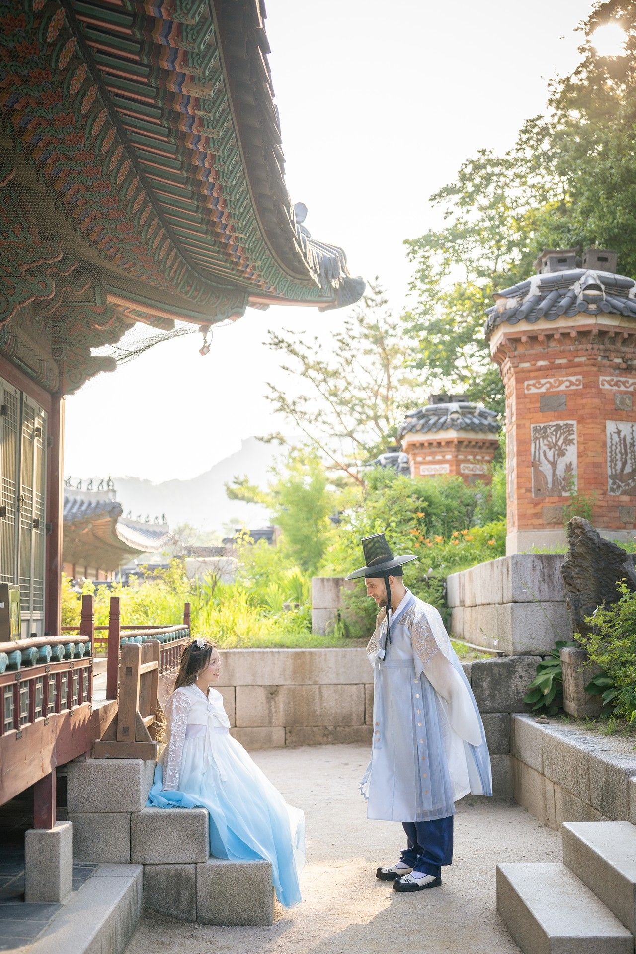 A couple in traditional Korean hanbok attire poses at a historic temple courtyard during sunset.