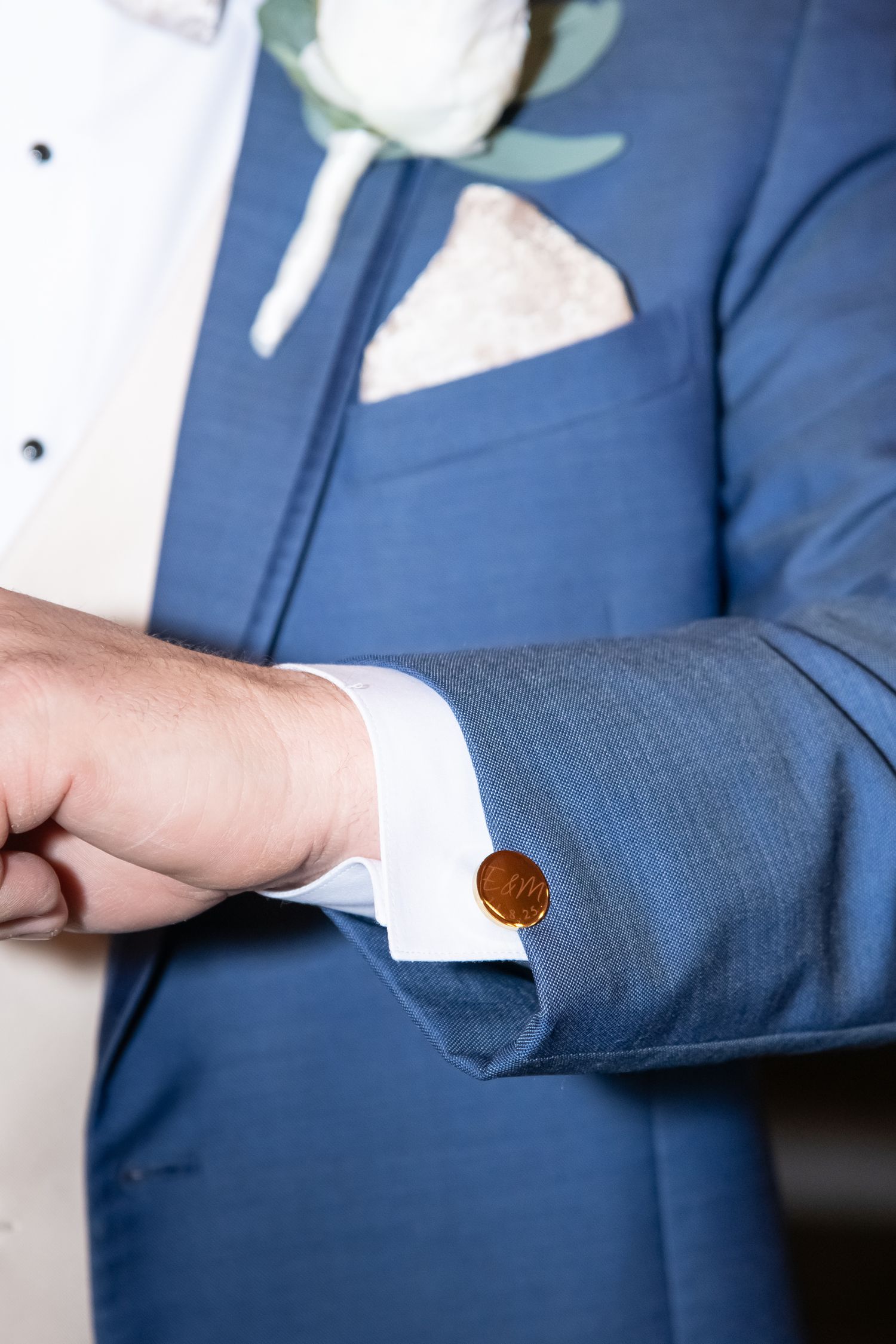 Professional in a navy blue suit jacket adjusts their sleeve cuff against a dark background.