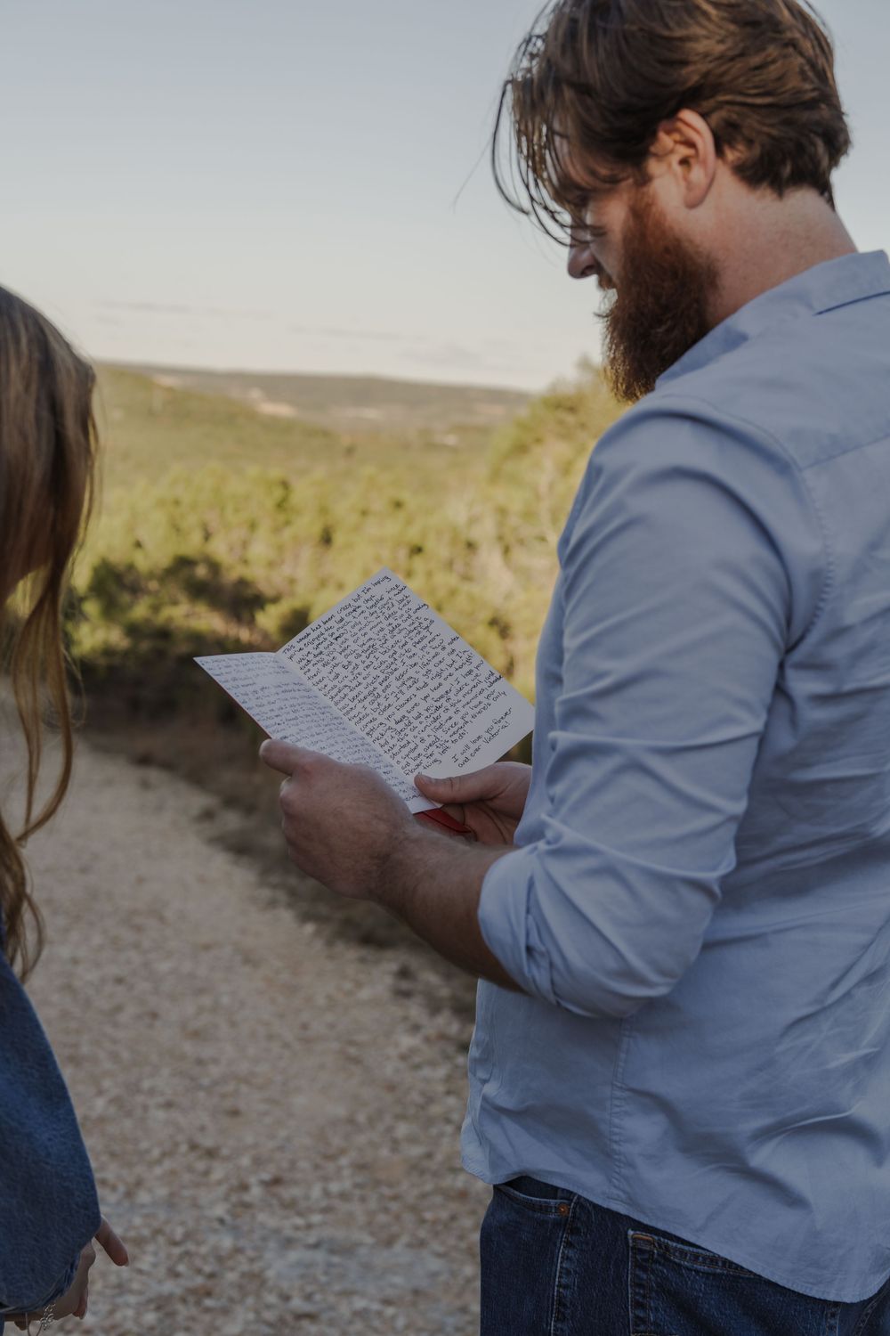 Couple reading letters together on a scenic hilltop at sunset.