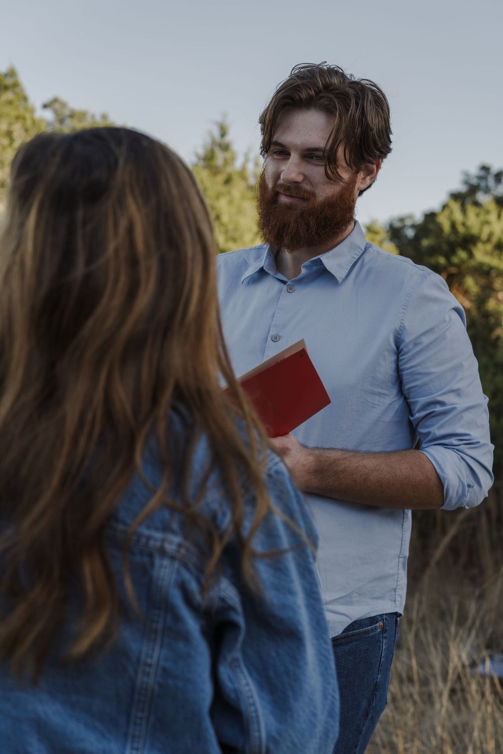 Couple in denim and blue button-down sharing emotional moment while reading letters outdoors.