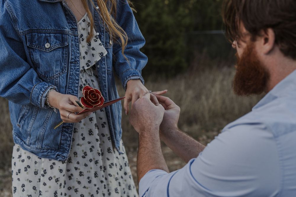 A close-up view of hands during a proposal moment while holding a red rose.