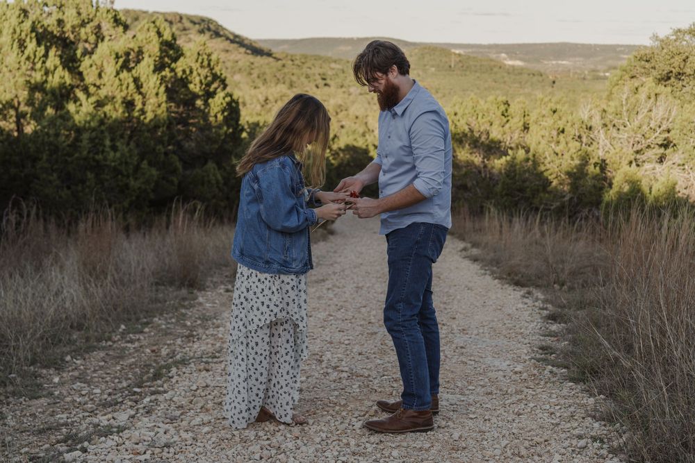 A couple looks at a ring together while standing on a rustic trail surrounded by nature.